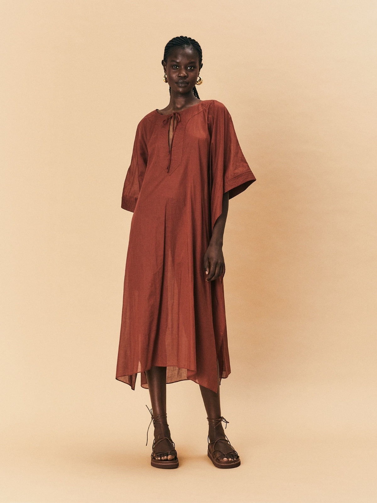 A woman wearing a brown La Maise Lia kaftan dress in brown against a beige background.