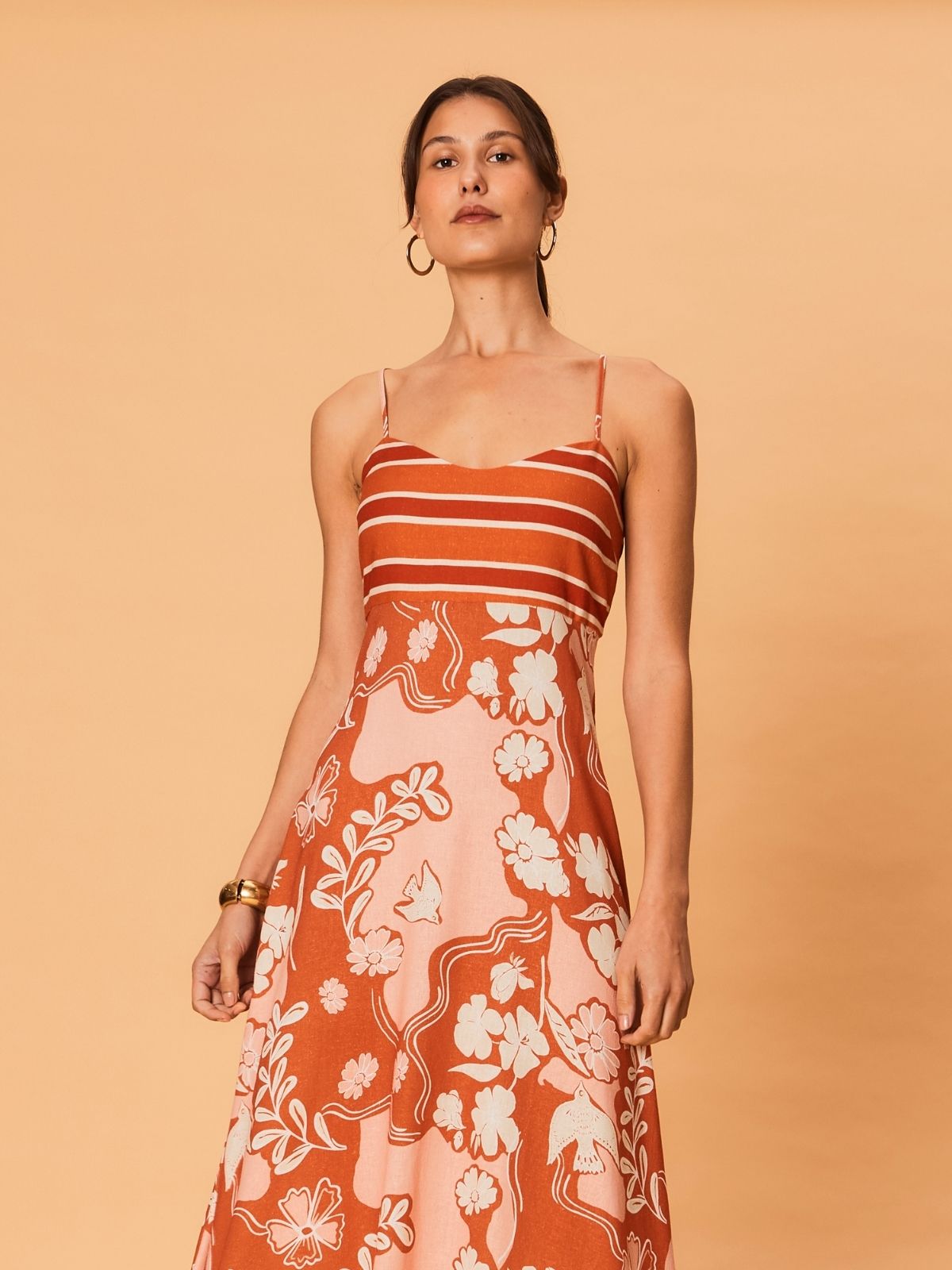 A young woman is wearing the Akira Maxi Dress by La Maise Studio, shown in close-up to highlight the thin shoulder straps, striped bodice, and delicate bird and floral print on lightweight fabric.
