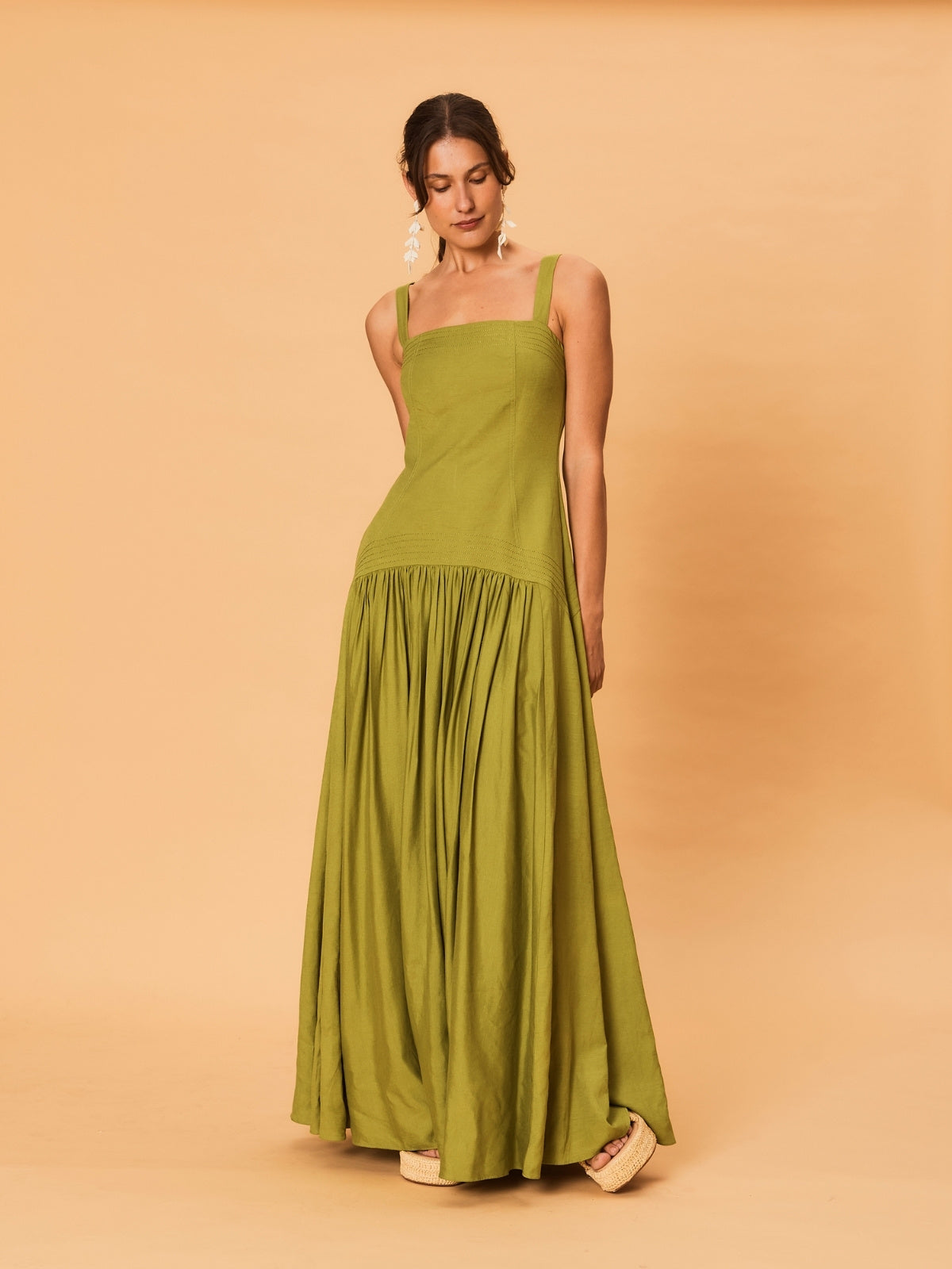A young woman wearing a green La Maise Verde Clare dress against a beige background.