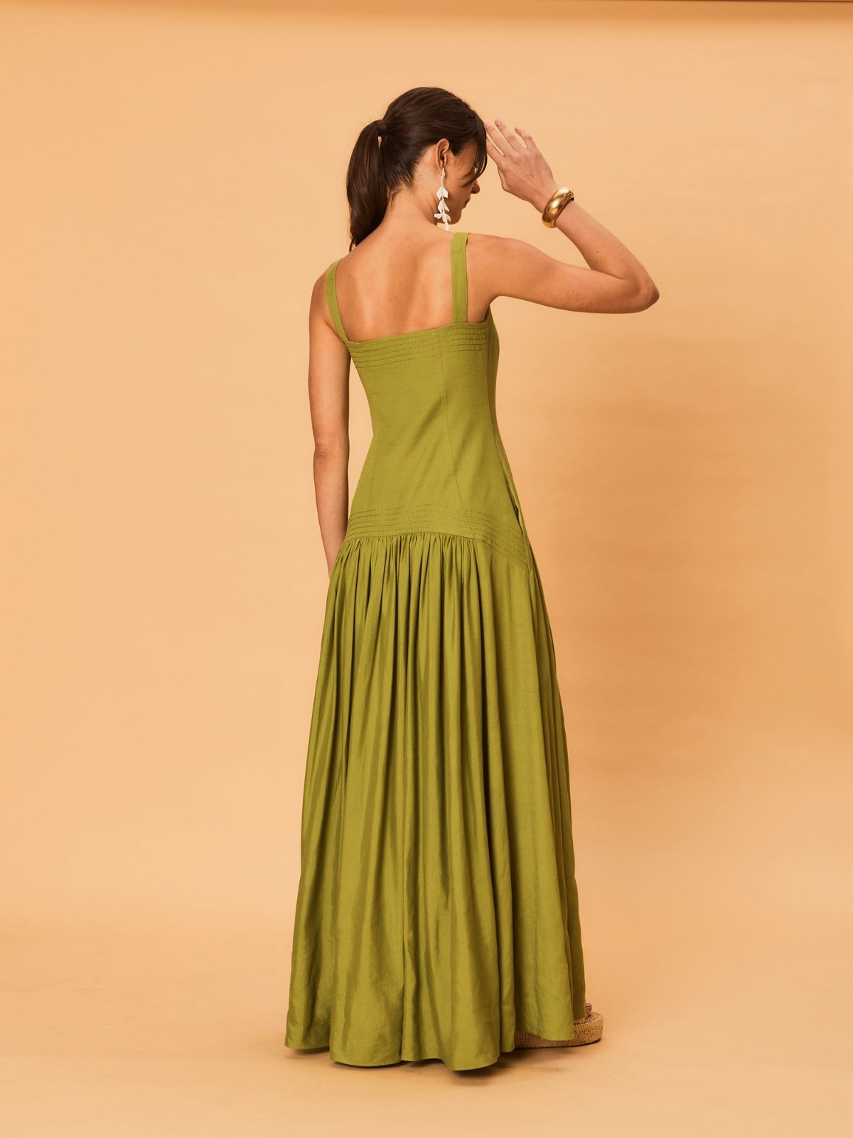 A young woman wearing a green La Maise Verde Clare dress against a beige background.