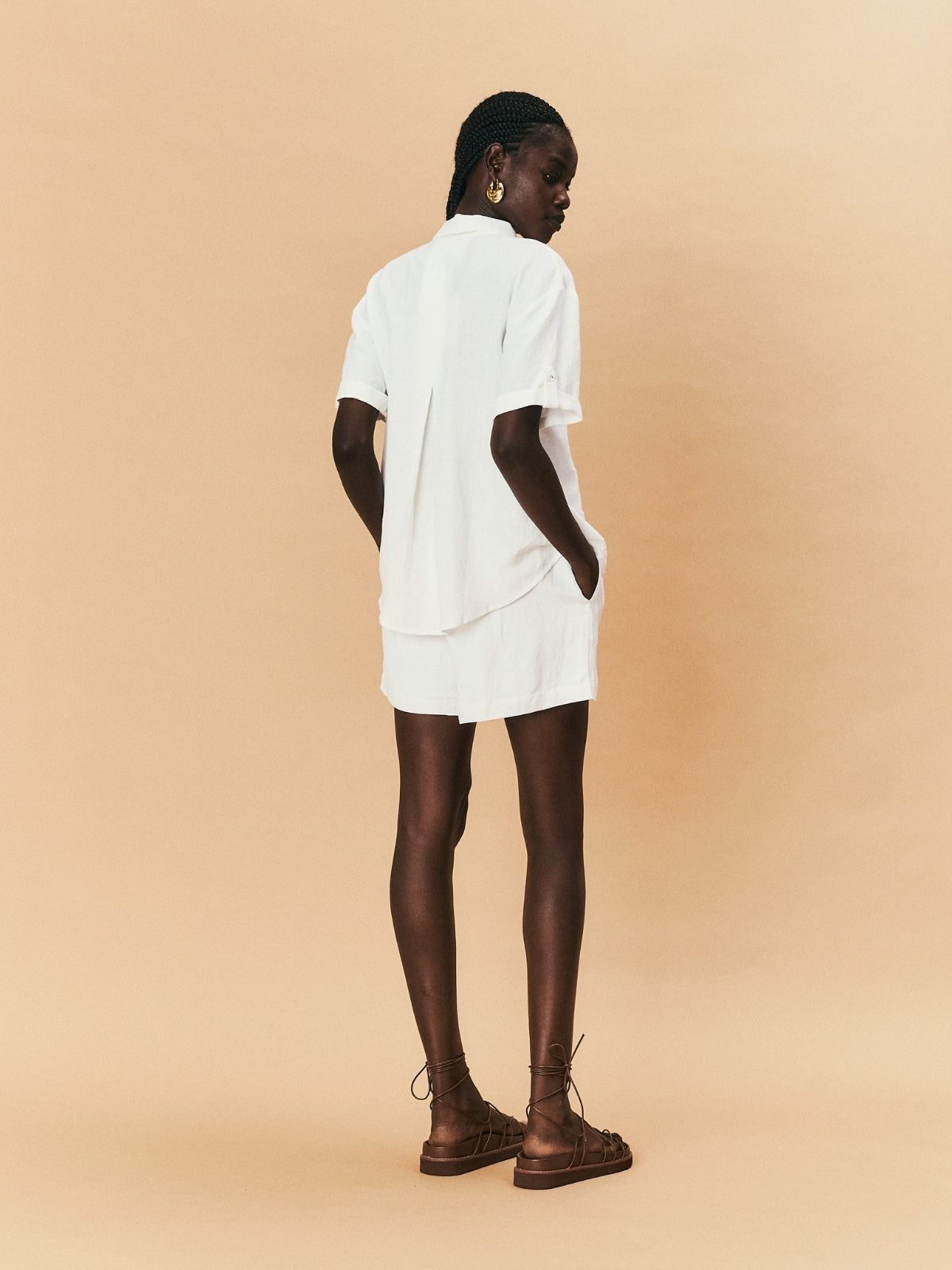 Person wearing a white outfit with brown boots on a beige background.