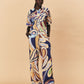 A woman wearing a colourful patterned La Maise Dijon pants with a shirt outfit on a beige background.