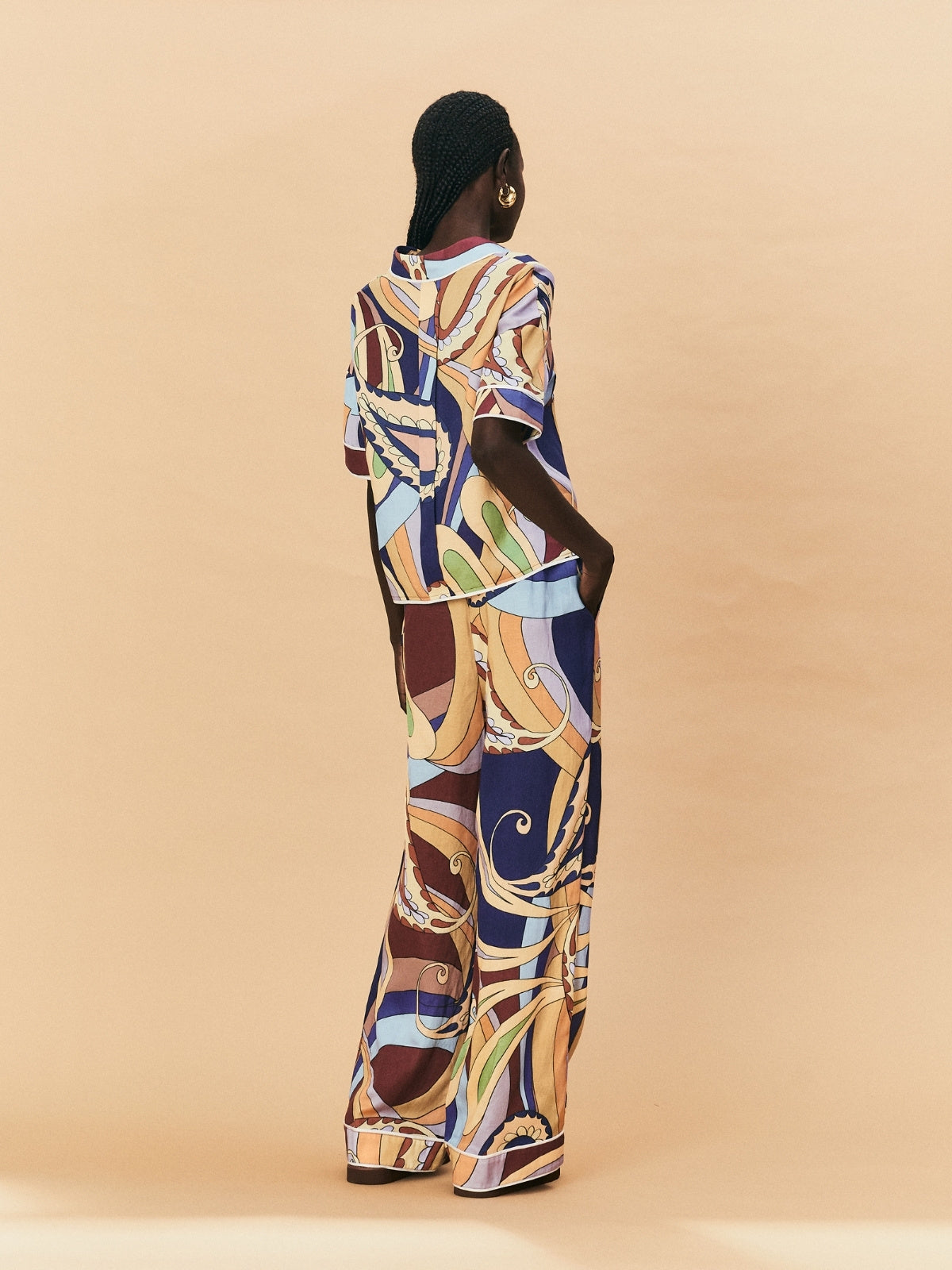 A woman wearing a colourful patterned La Maise Dijon pants with a shirt outfit on a beige background.