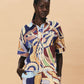 A young woman wearing a colourful patterned La Maise dijon shirt paisly print on a beige background.