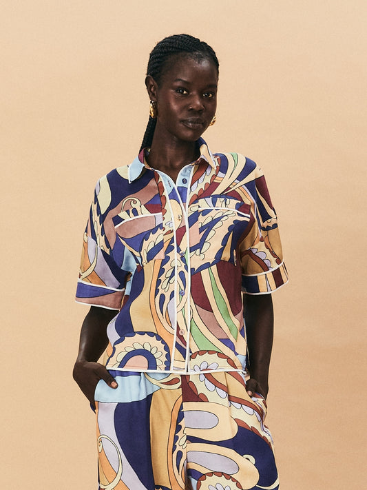 A young woman wearing a colourful patterned La Maise dijon shirt paisly print on a beige background.