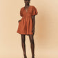 Woman wearing a rust-colored La Maise Le Havre romper against a beige background.