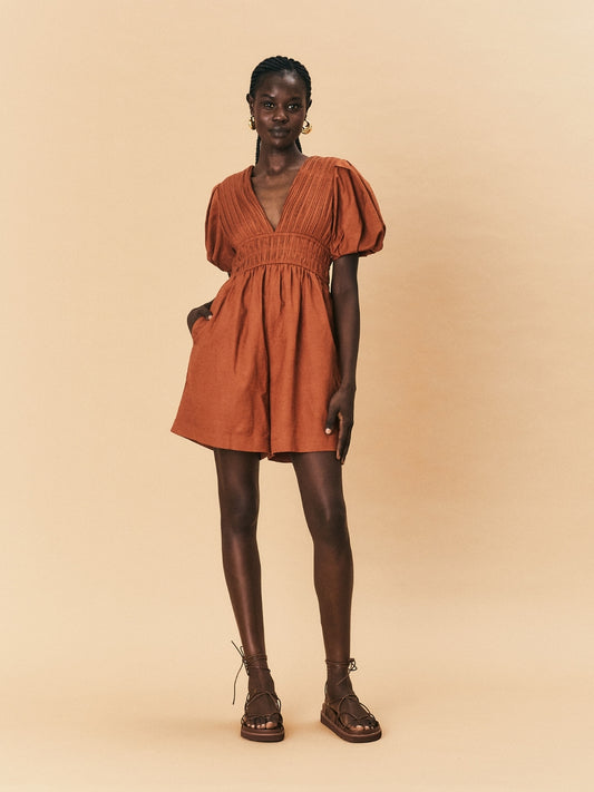 Woman wearing a rust-colored La Maise Le Havre romper against a beige background.