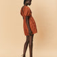 Woman wearing a rust-colored dress and brown shoes on a beige background