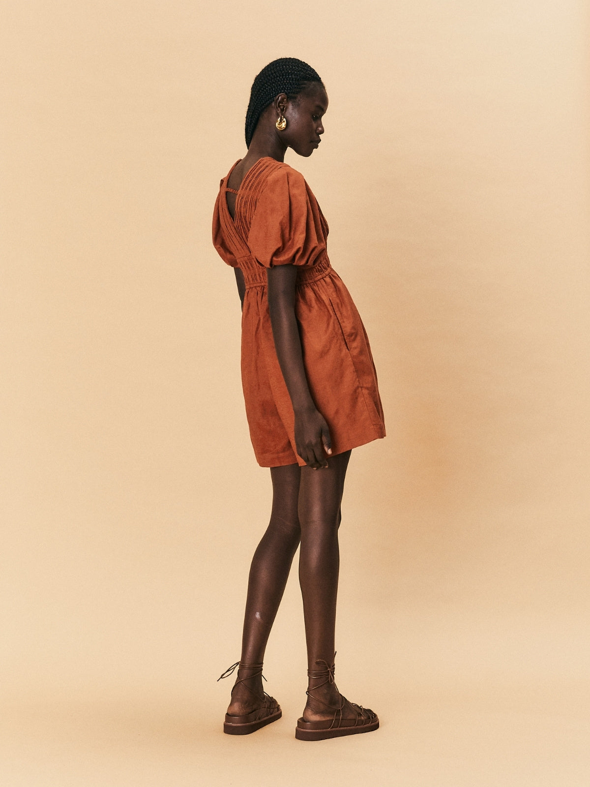 Woman wearing a rust-colored dress and brown shoes on a beige background