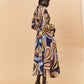 A young woman wearing a colourful patterned La Maise Dijon maxi shirt dress on a beige background.
