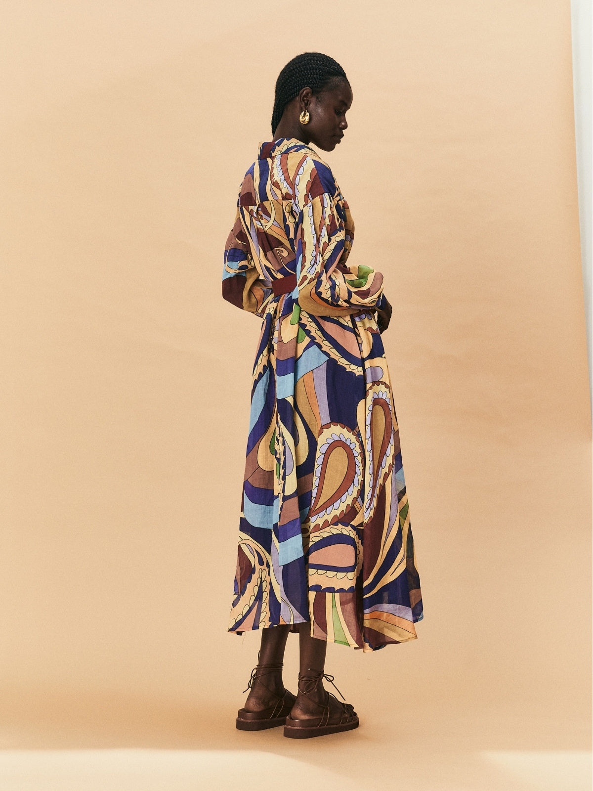 A young woman wearing a colourful patterned La Maise Dijon maxi shirt dress on a beige background.