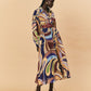 A young woman wearing a colourful patterned La Maise Dijon maxi shirt dress on a beige background.