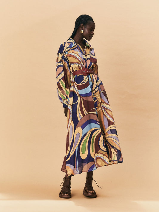 A young woman wearing a colourful patterned La Maise Dijon maxi shirt dress on a beige background.