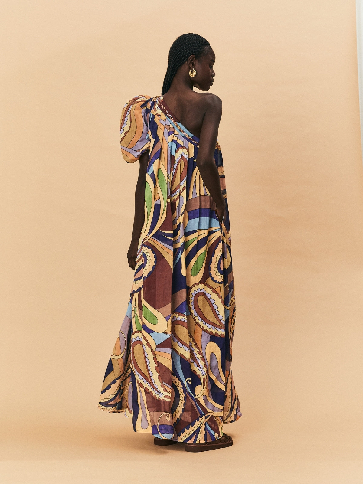 A woman wearing a one-shoulder, La Maise Dijon maxi dress on a beige background.