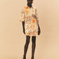 A young woman wearing a La Maise mini dress with seashell print on a beige background.