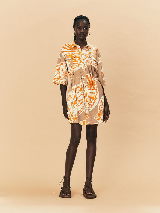 A young woman wearing a La Maise mini dress with seashell print on a beige background.