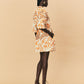 Woman wearing a patterned dress with sheer overlay on a beige background.