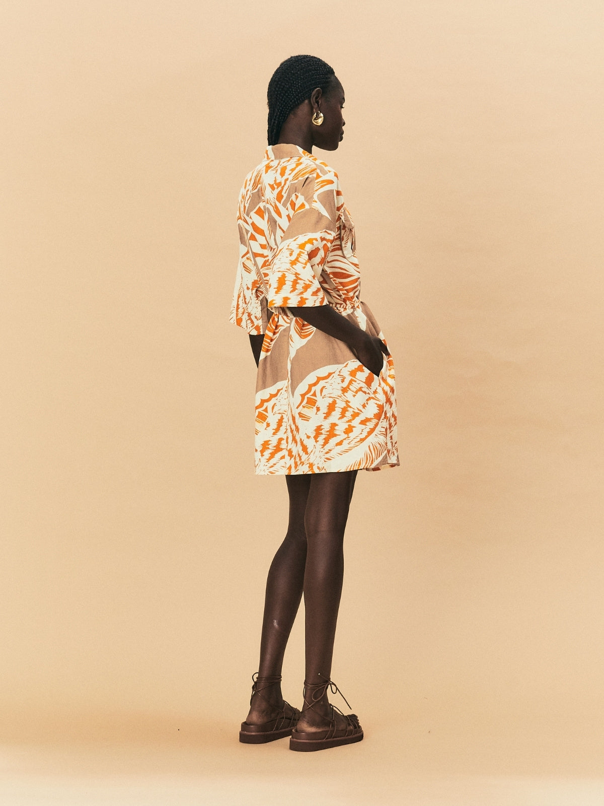 Woman wearing a patterned dress with sheer overlay on a beige background.