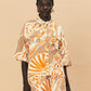 A young woman wearing La Maise Cannes shirt with seashell print on beige background.
