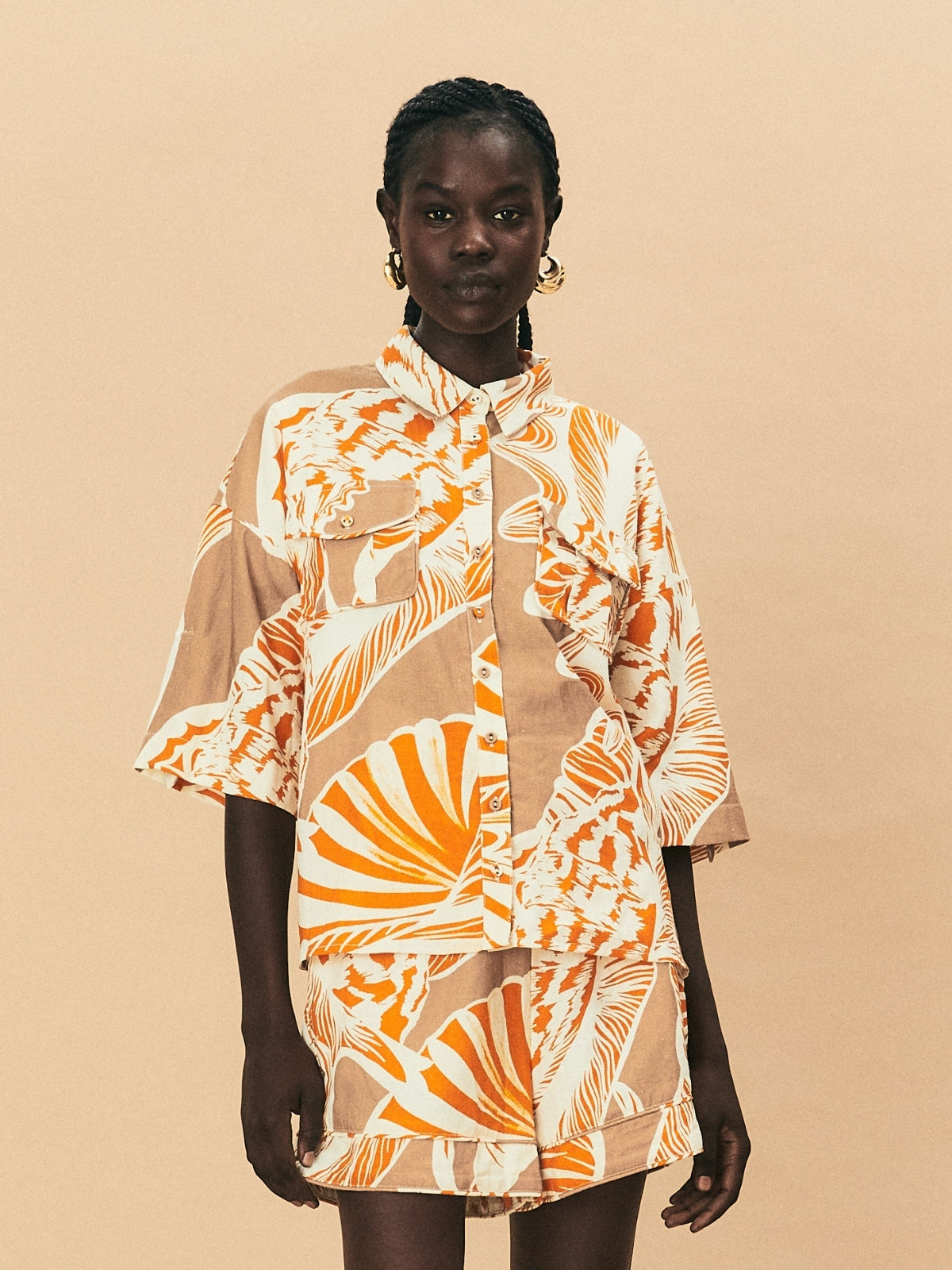 A young woman wearing La Maise Cannes shirt with seashell print on beige background.