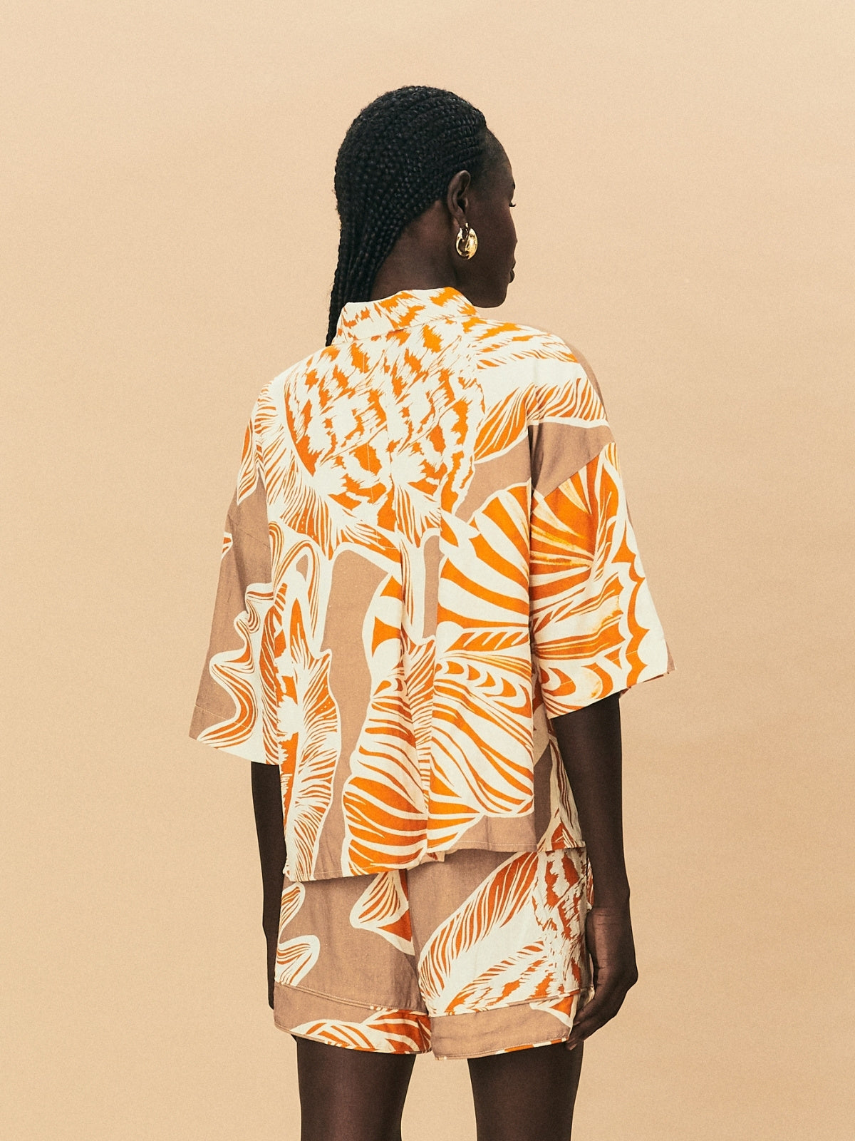 A young woman wearing La Maise Cannes shirt with seashell print on beige background.