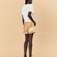 A woman wearing La Maise Cannes shorts  with seashell print on a beige background.
