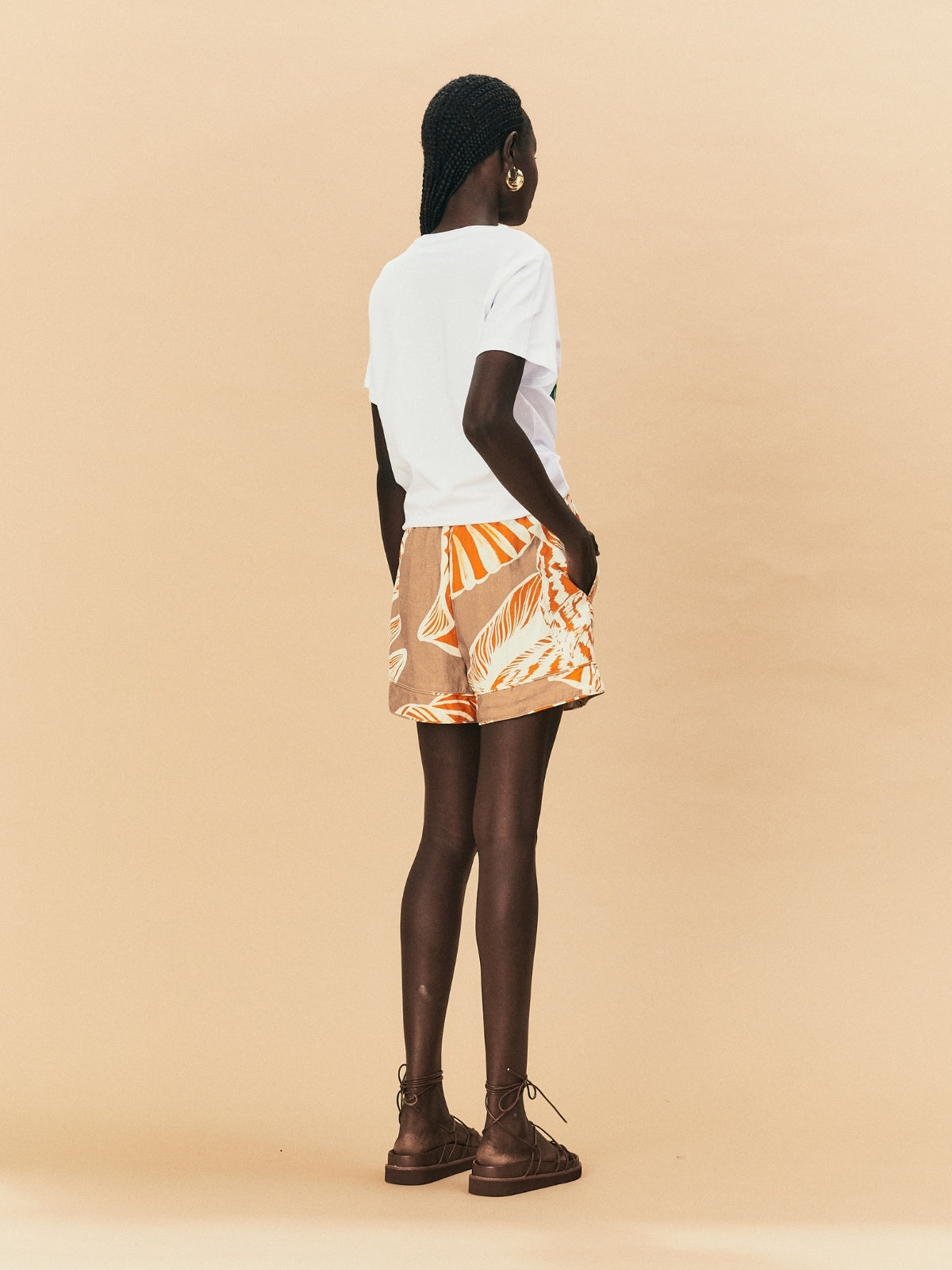 A woman wearing La Maise Cannes shorts  with seashell print on a beige background.