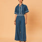 A young woman wearing La Maise Ellie wide leg jean in indigo with lace trim  on a beige background.