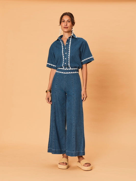 A young woman wearing La Maise Ellie wide leg jean in indigo with lace trim  on a beige background.