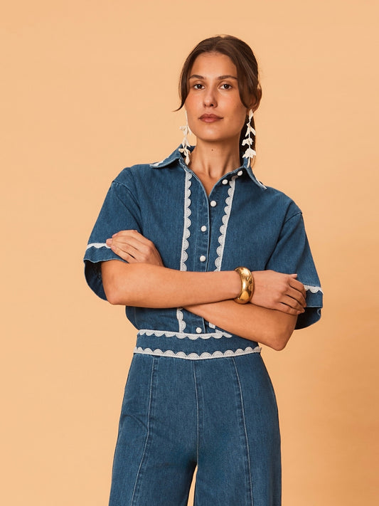 A young woman wearing La Maise Ellie denim shirt in blue denim with white lace trim on a beige background.