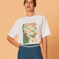 A young woman wearing a white La Maise Great Barrier Reef  tee on a beige background.