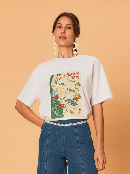 A young woman wearing a white La Maise Great Barrier Reef  tee on a beige background.