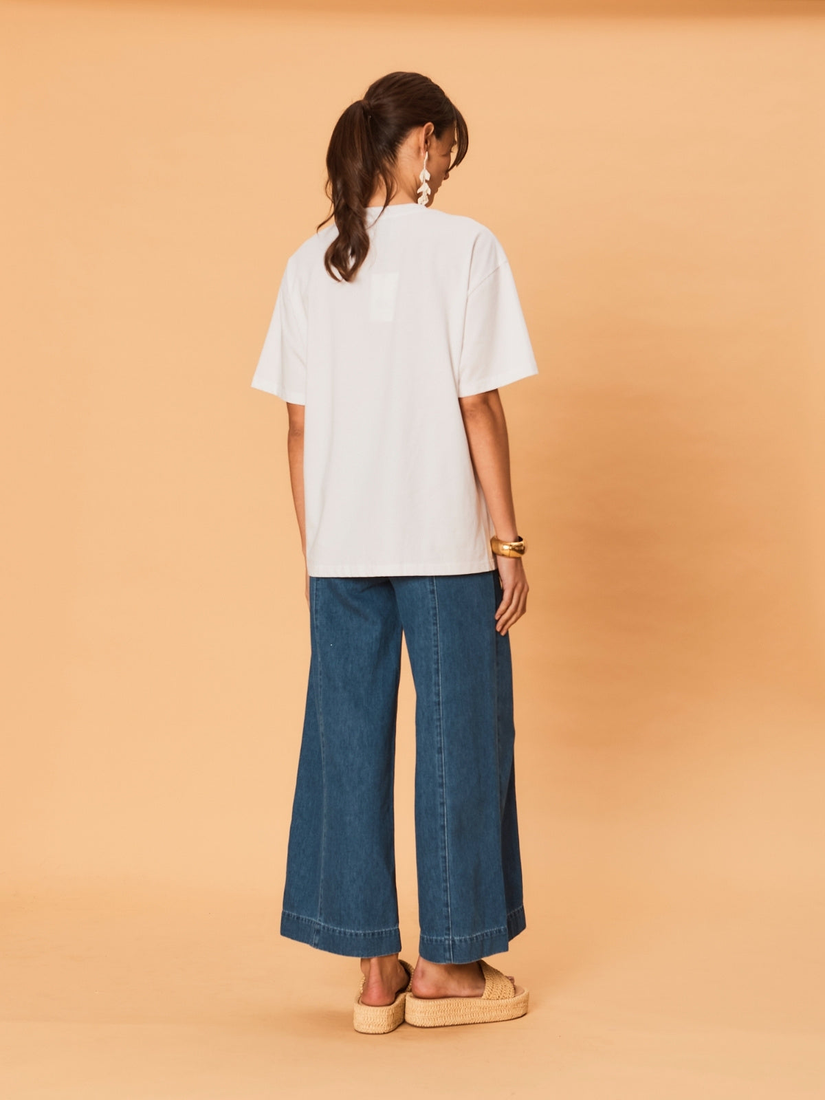 Person wearing a white t-shirt and blue jeans on a beige background