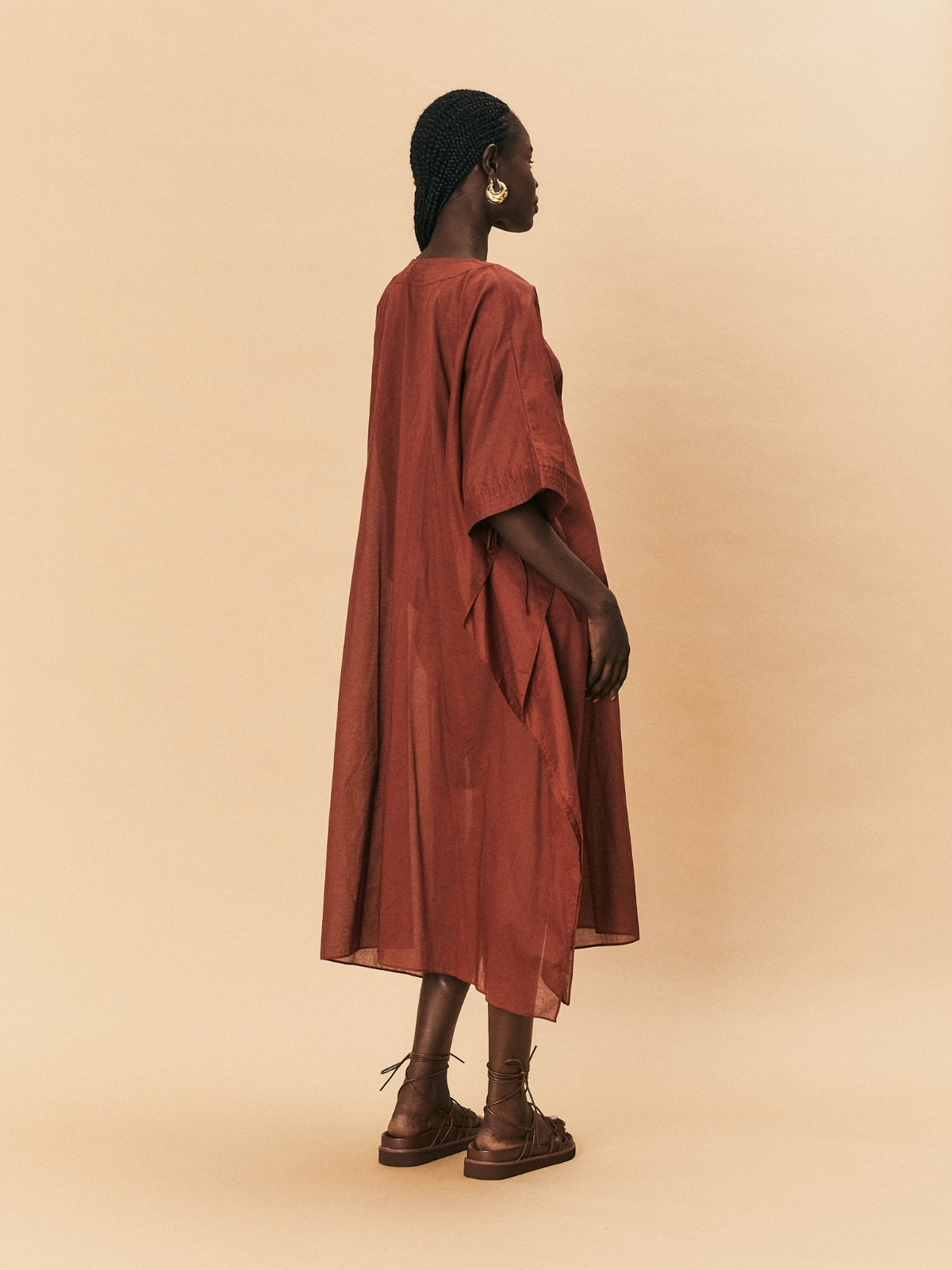 Person wearing a long rust-colored dress against a beige background
