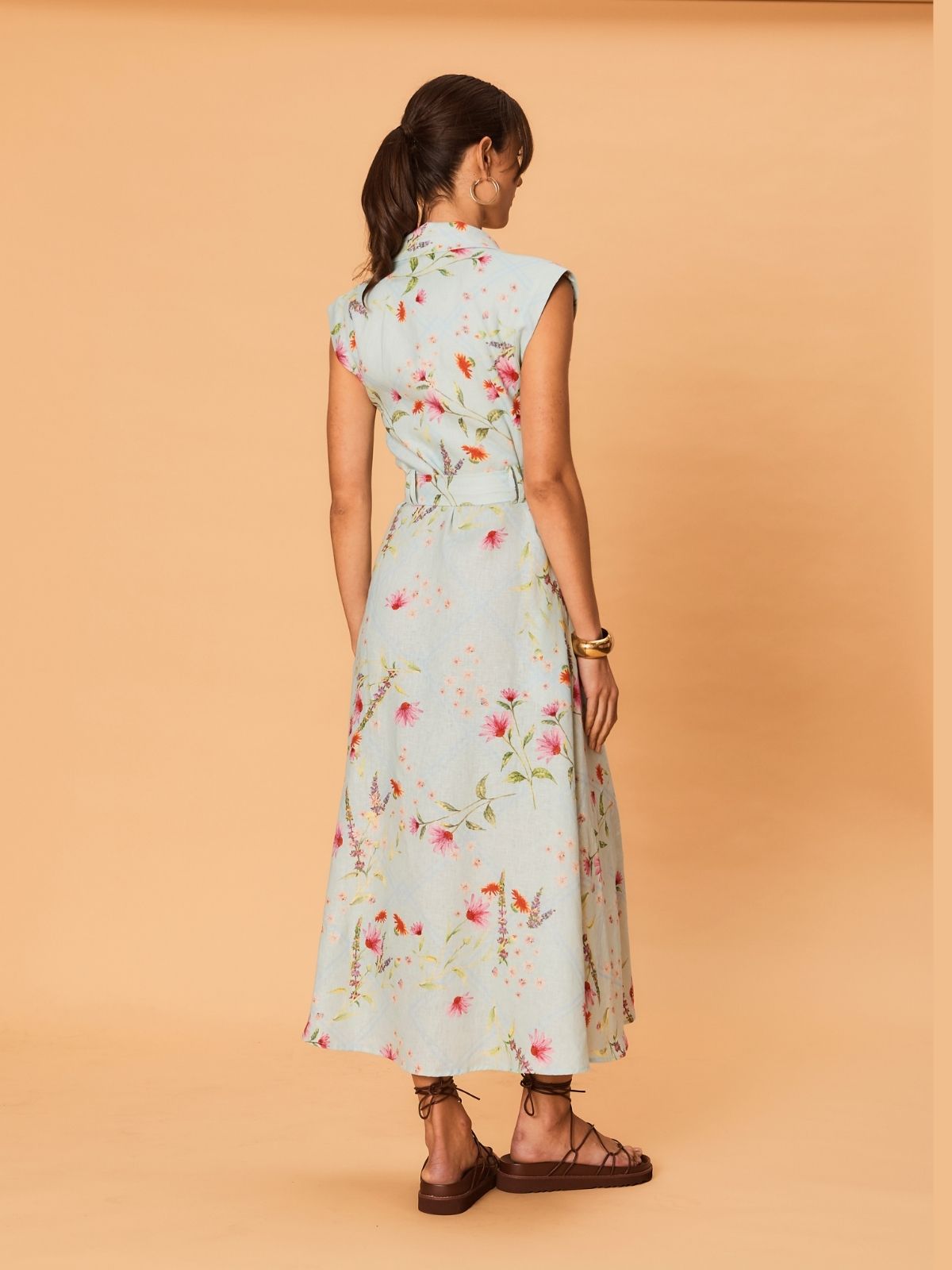 Back view of sleeveless floral midi dress with fitted waist and flowing skirt, worn with flat sandals.