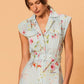 Close-up of floral linen midi dress showing tailored waist, fabric belt and button detailing on soft blue background.