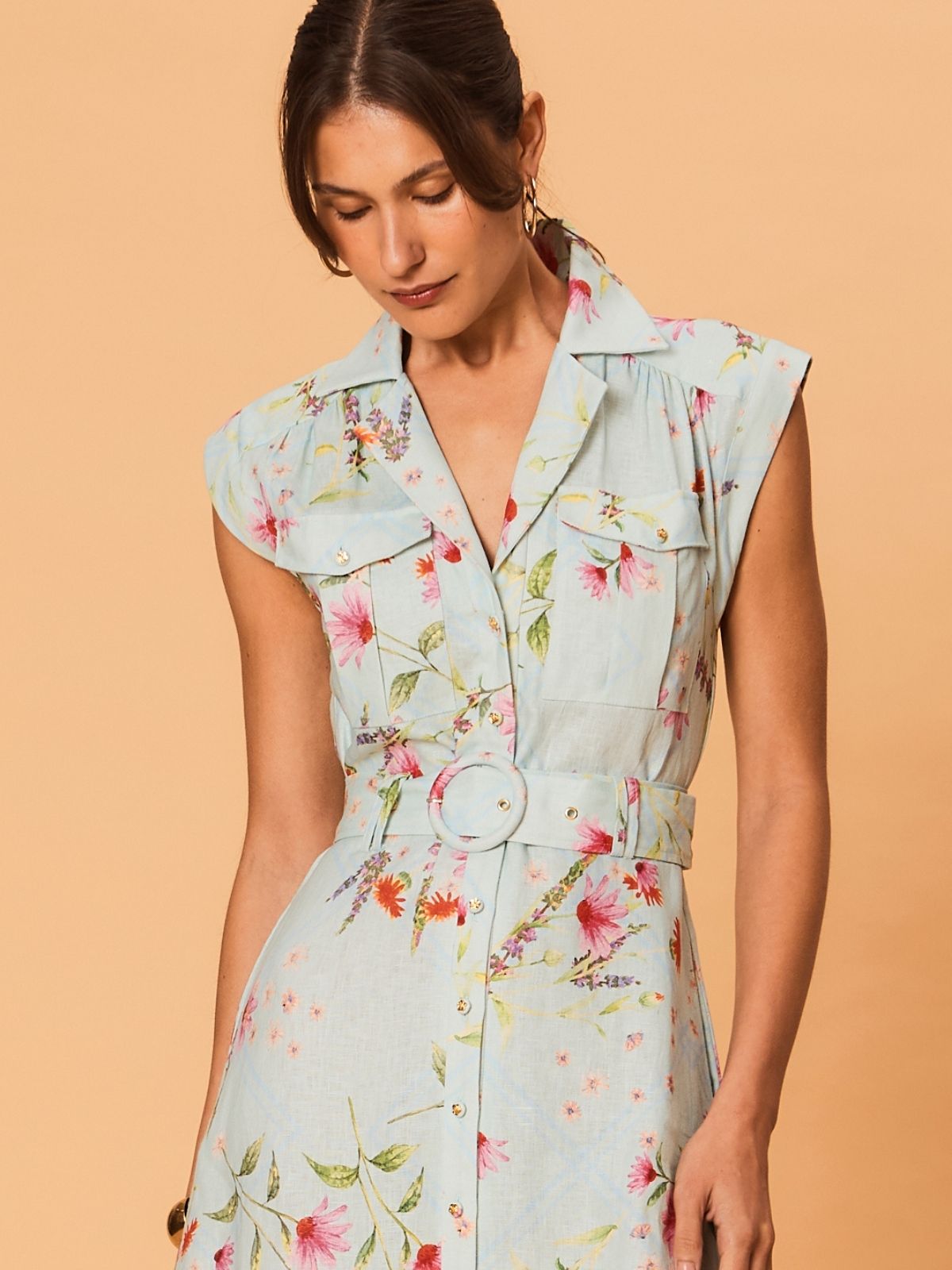 Close-up of floral linen midi dress showing tailored waist, fabric belt and button detailing on soft blue background.