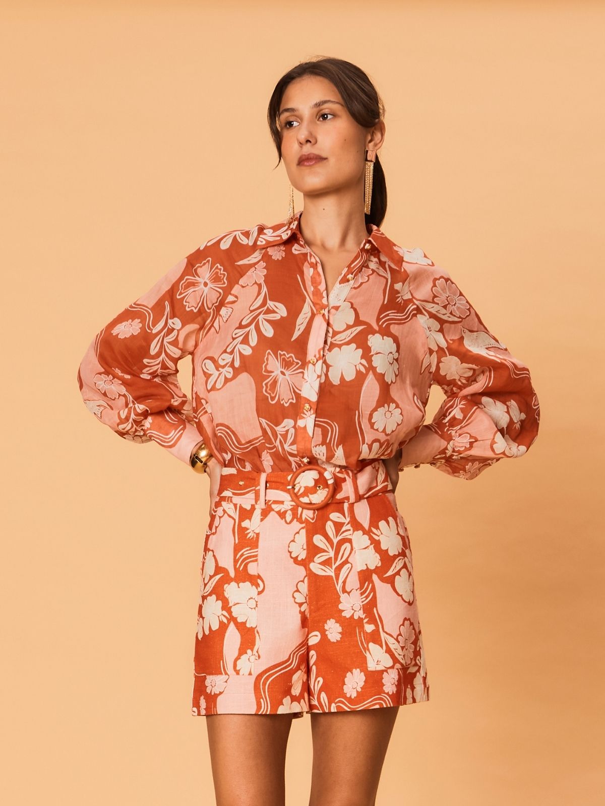 A model wears the Akira Blouse by La Maise Studio, featuring a terracotta and blush bird floral print with a button-front design.