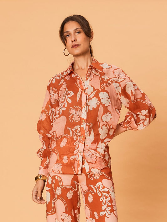 A young woman wearing the Akira Blouse by La Maise Studio, featuring a terracotta and blush bird and floral print, long sleeves and a button-front design, styled with matching printed shorts.