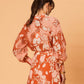 Rear view of a woman wearing the Akira Blouse by La Maise Studio, showing the flowing ramie fabric, long sleeves and bird floral pattern across the back.