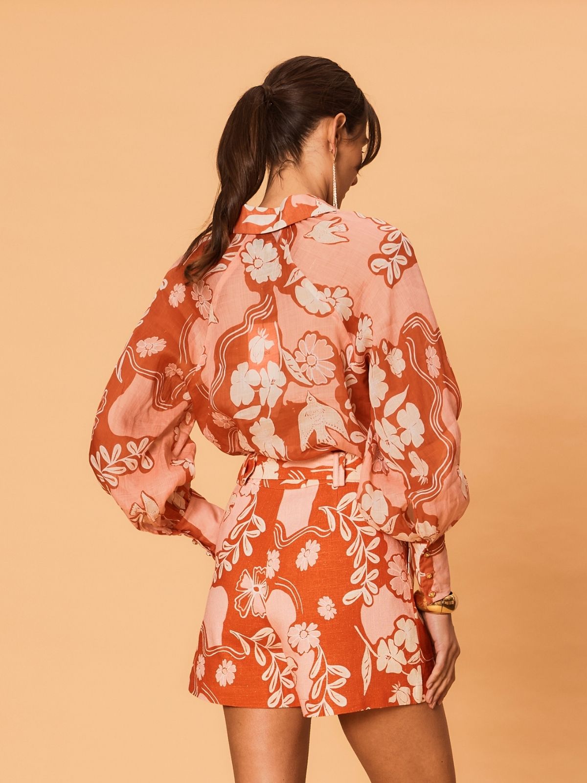 Rear view of a woman wearing the Akira Blouse by La Maise Studio, showing the flowing ramie fabric, long sleeves and bird floral pattern across the back.