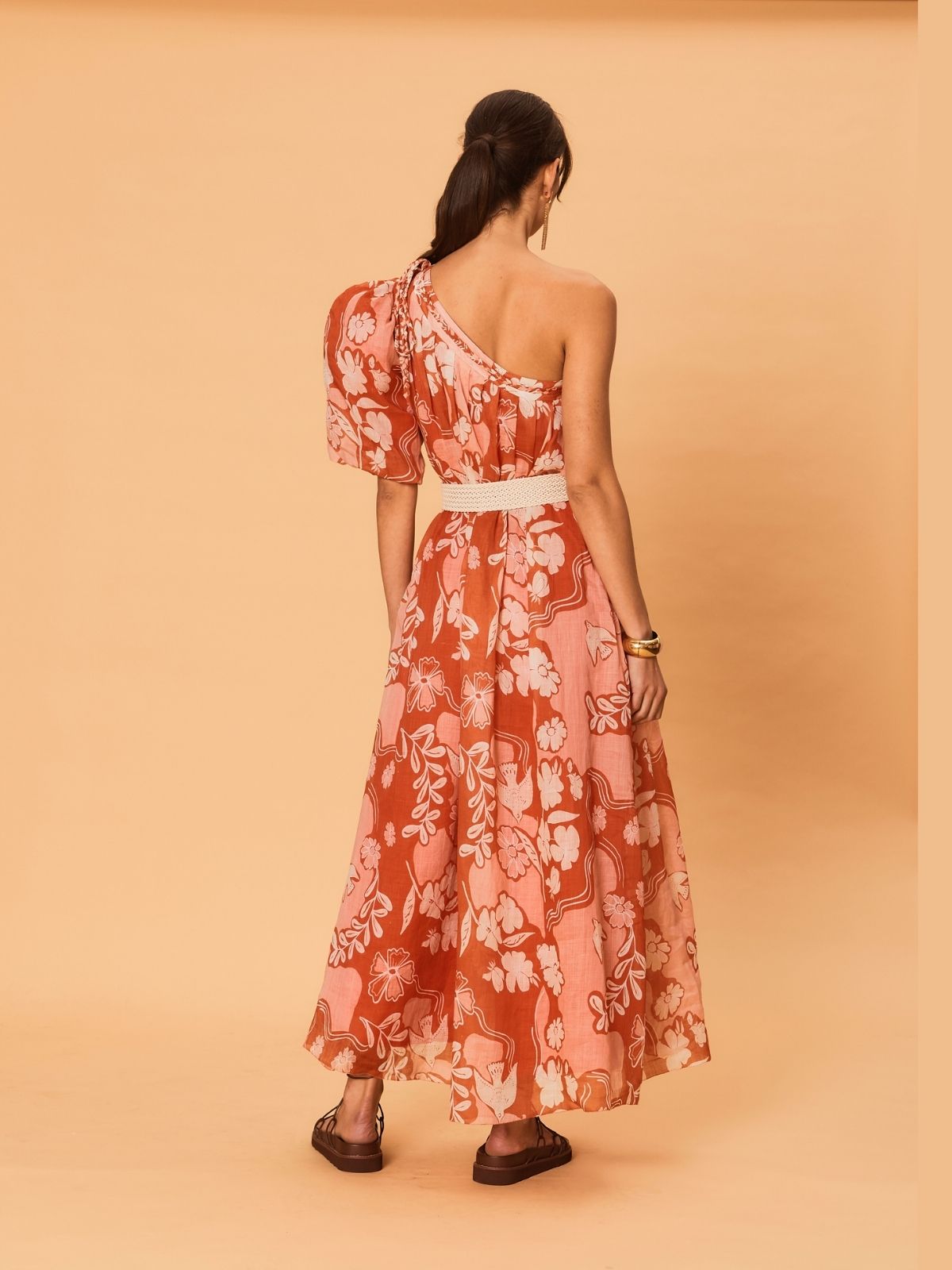 A back view of a woman wearing the La Maise Studio Akira One Shoulder Dress in bird floral print, showing the open shoulder line, soft gathering, and fluid skirt movement.