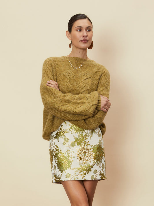 Model wearing the Dahlia floral mini skirt in green tones, styled with with olive knit jmper against a neutral studio backdrop