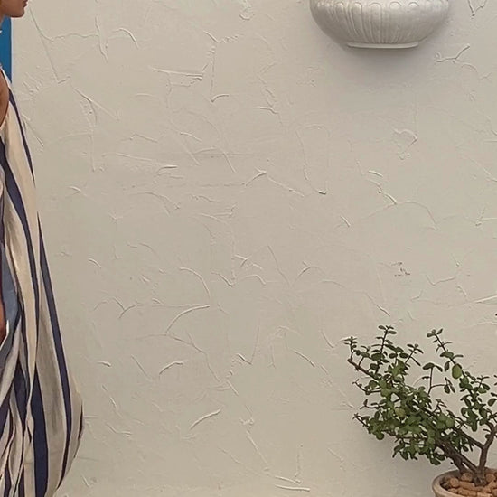 A video showing a young woman wearing the Mila Maxi Dress – Stripe by La Maise Studio, featuring a sleeveless high-neck design with vertical navy and cream stripes and a flowing maxi-length silhouette.